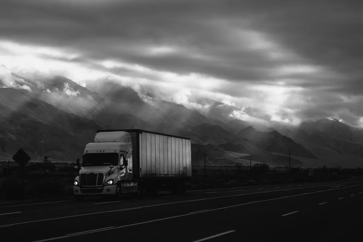 A white trailer truck traveling along a road, photographed by Robson Hatsukami Morgan.